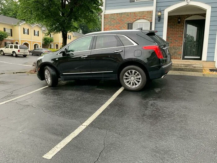 A black SUV parked incorrectly across a parking space line, an example of neighbors bad parking.