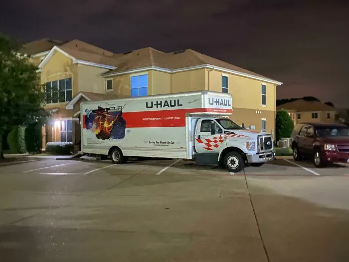 A large U-Haul moving truck occupying multiple parking spots in an apartment complex at night, demonstrating bad parking.