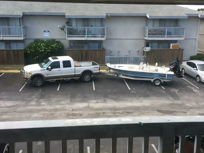 A large truck with a boat trailer taking up multiple parking spaces, showing a lack of common sense by jerk neighbors.