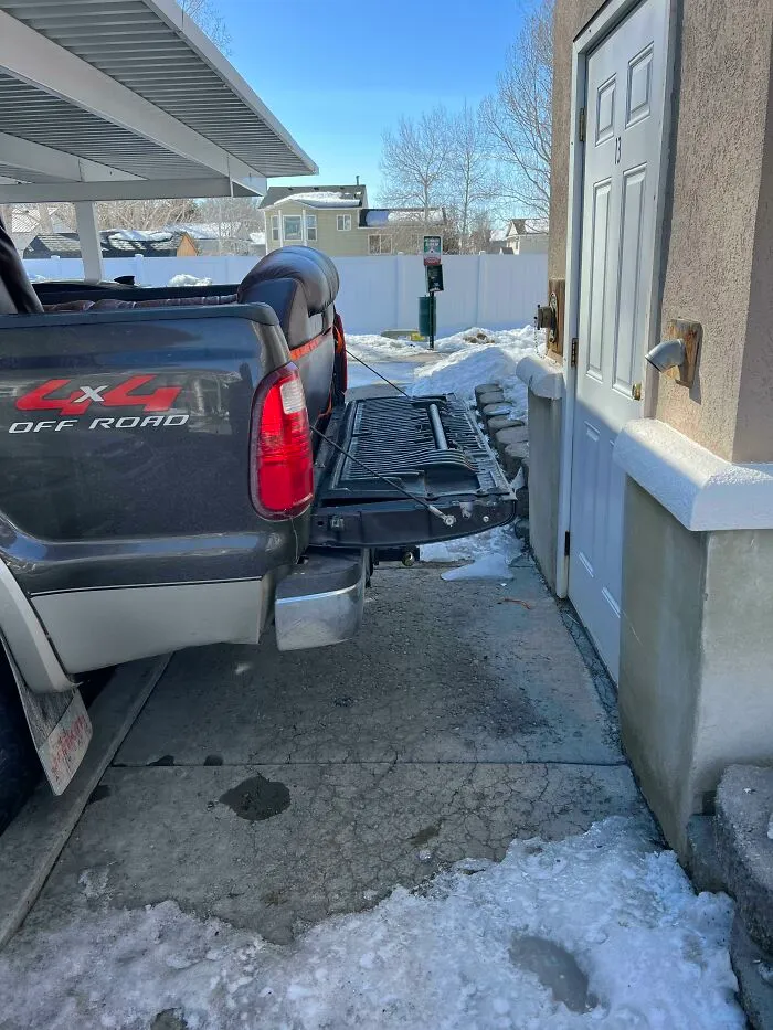A pickup truck with its tailgate down blocking a doorway, illustrating inconsiderate parking by jerk neighbors.