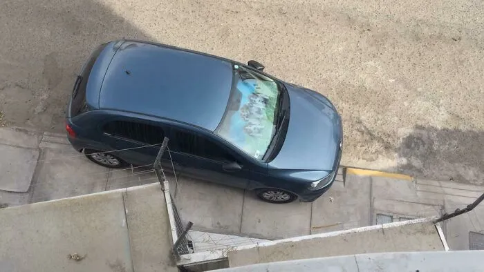 A blue car showing an urgent parking lesson, parked diagonally across a curb and sidewalk from an aerial view.
