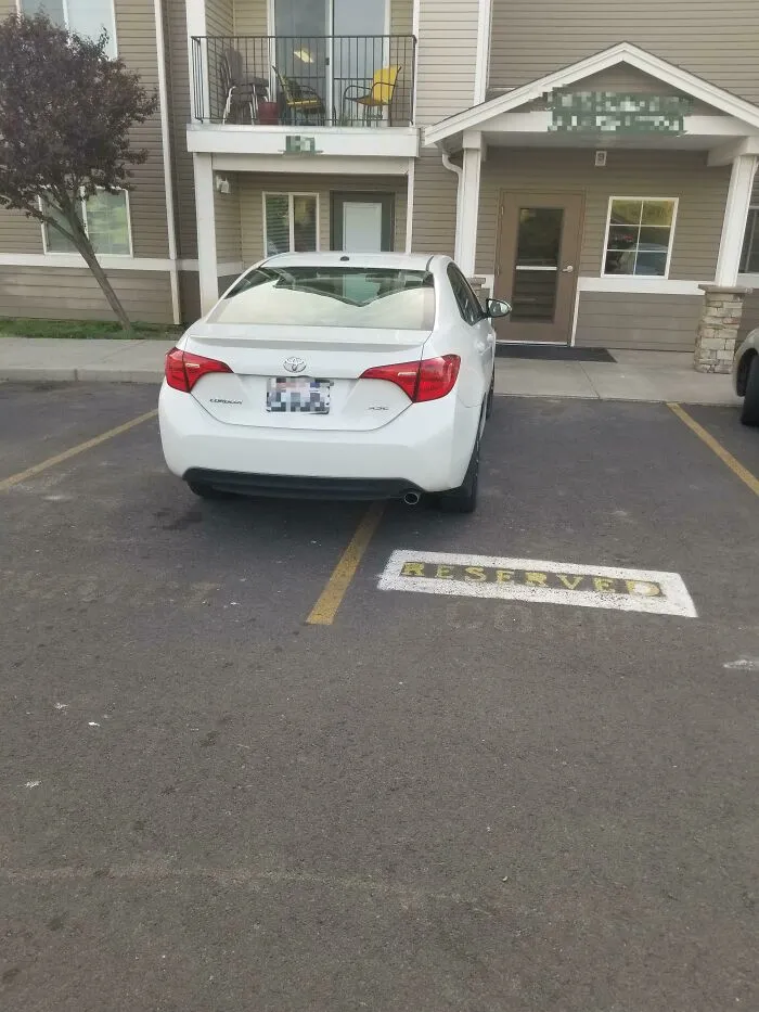 A white car poorly parked across a reserved parking spot, demonstrating a neighbor's bad parking.