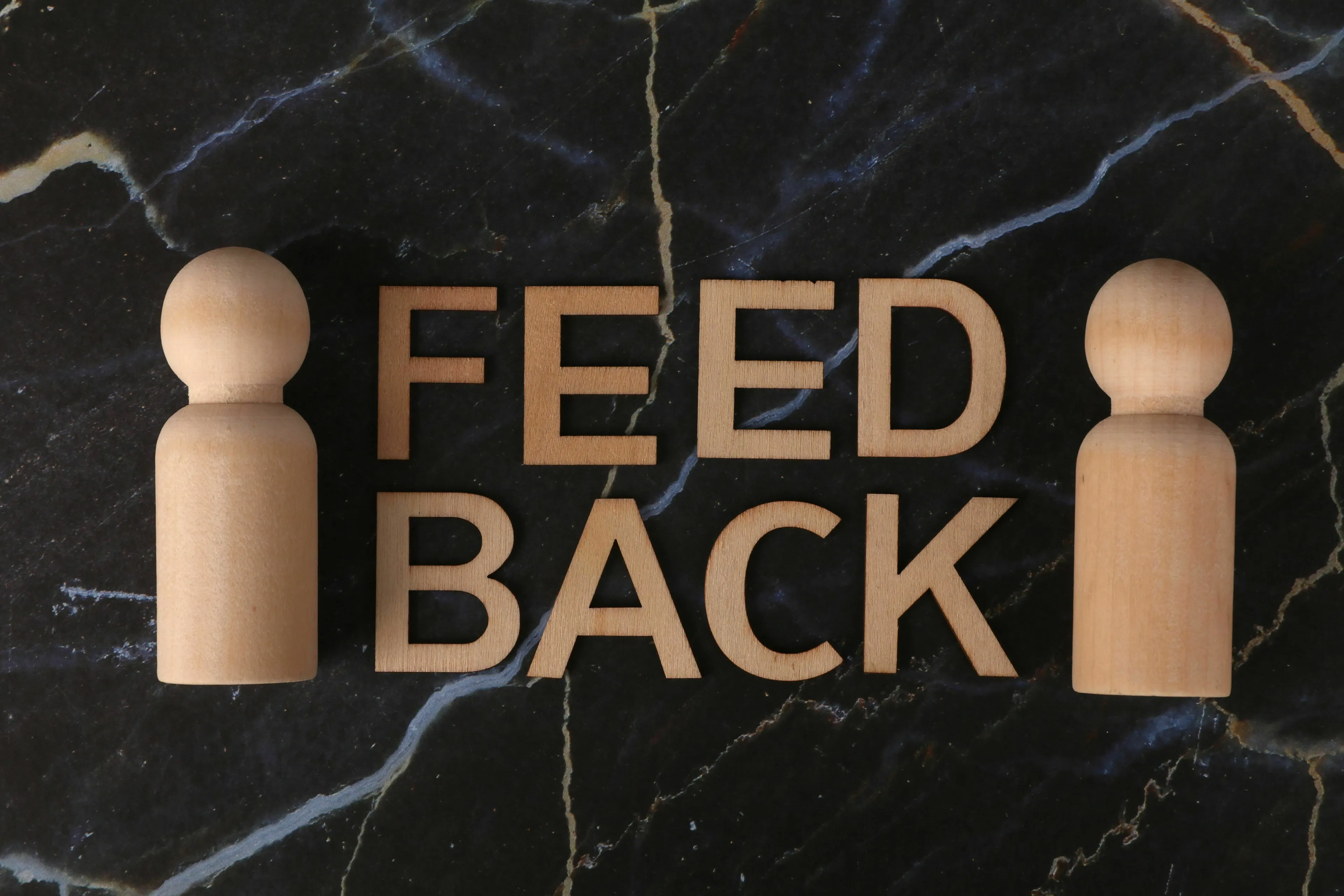 The word FEEDBACK spelled out in wooden letters between two wooden human figures on a marble background. What kind of liar are you when giving feedback?