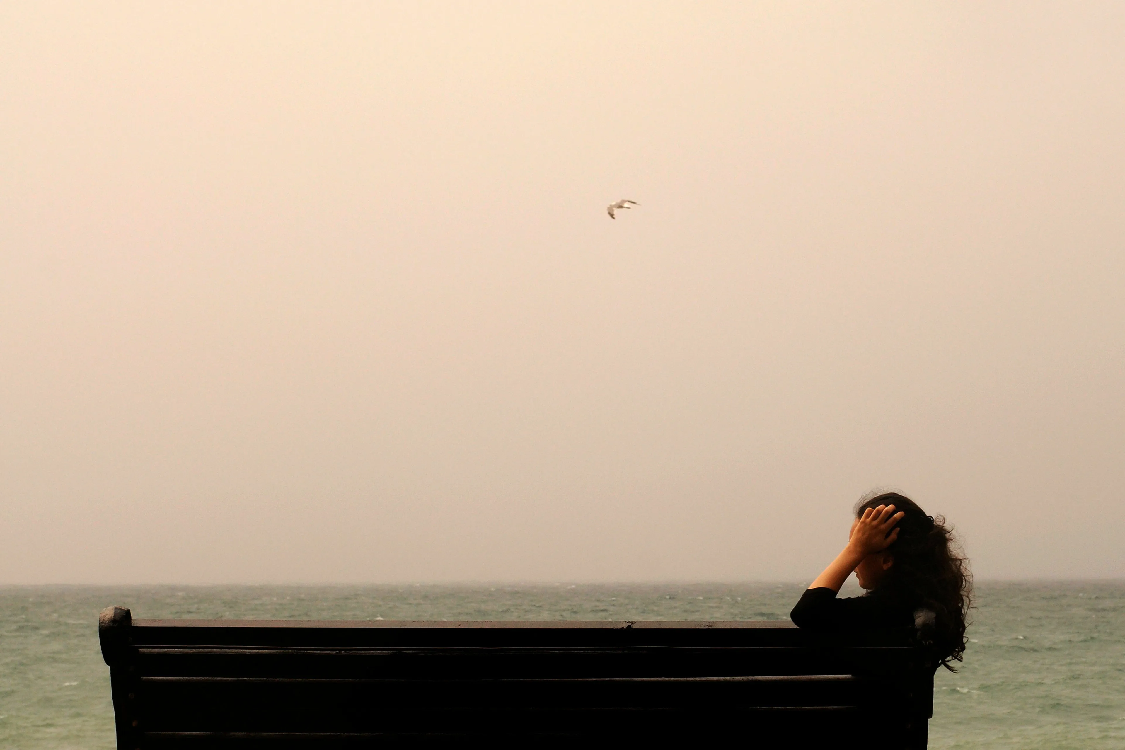 A woman sits by the ocean, contemplating how to handle not knowing something everyone else knows.