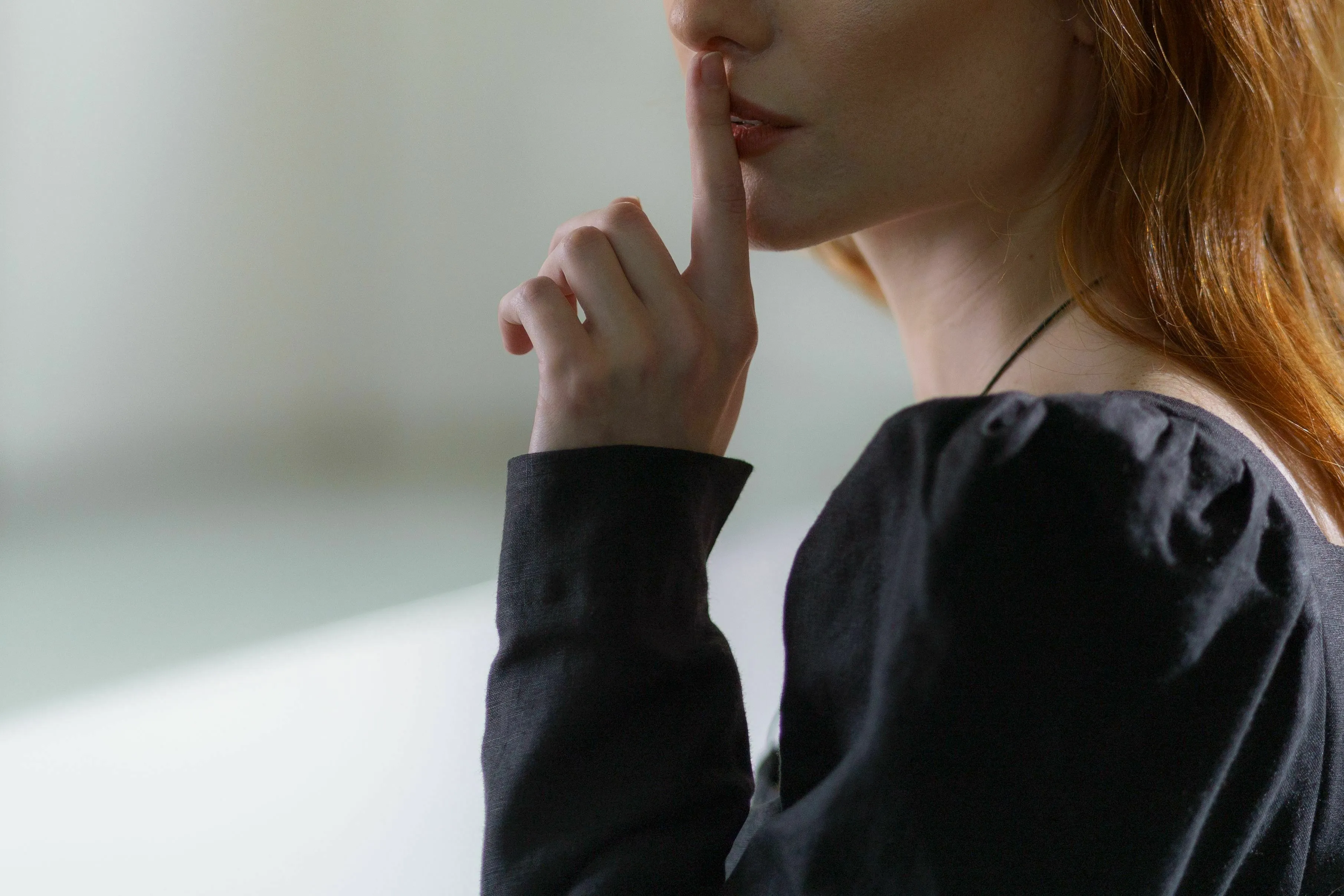 A woman with red hair and a black shirt holding a finger to her lips, signifying silence. What kind of liar are you?