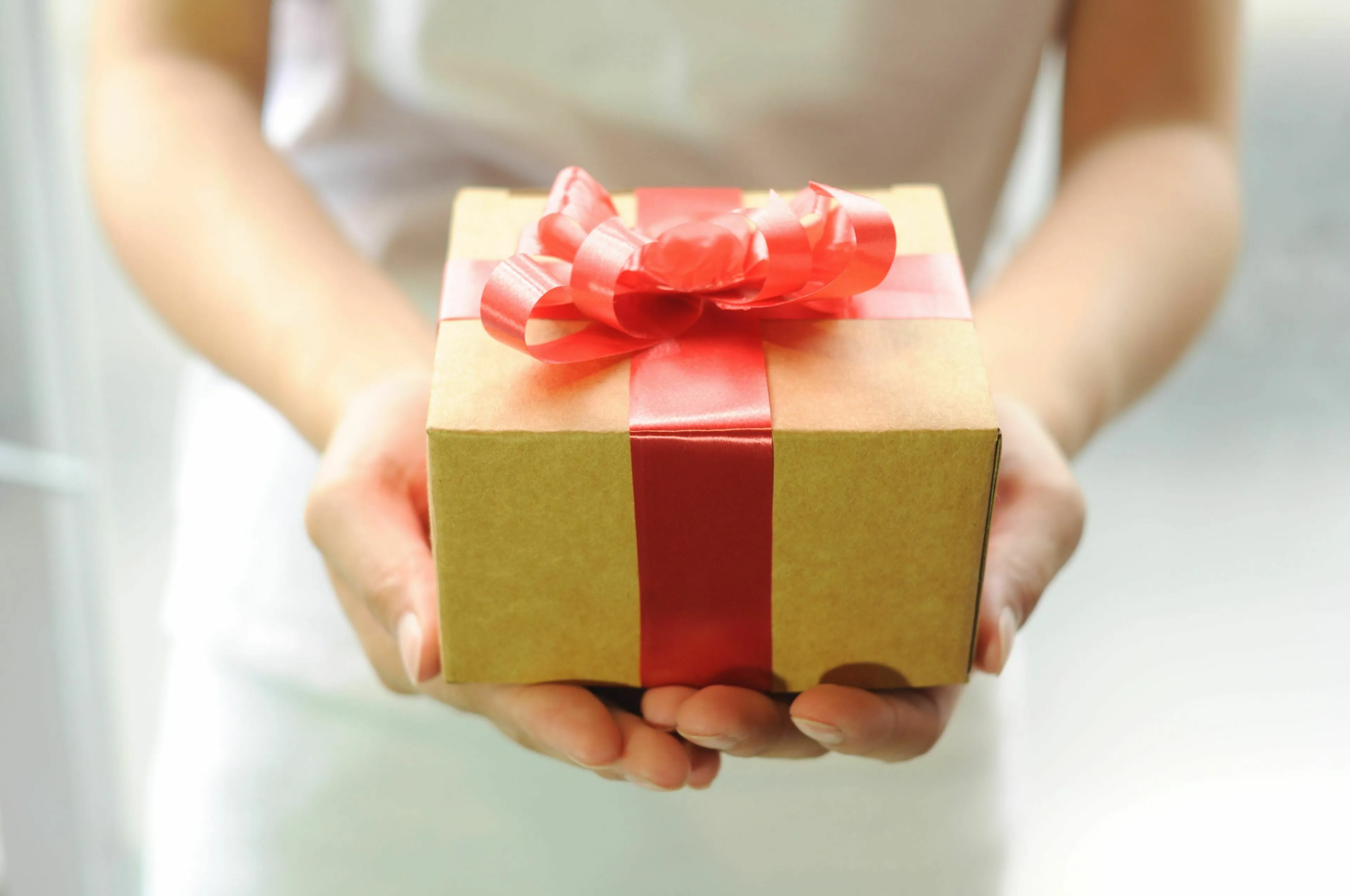 Hands presenting a wrapped gift with a red ribbon, representing what happens when you don't like the gift you got.