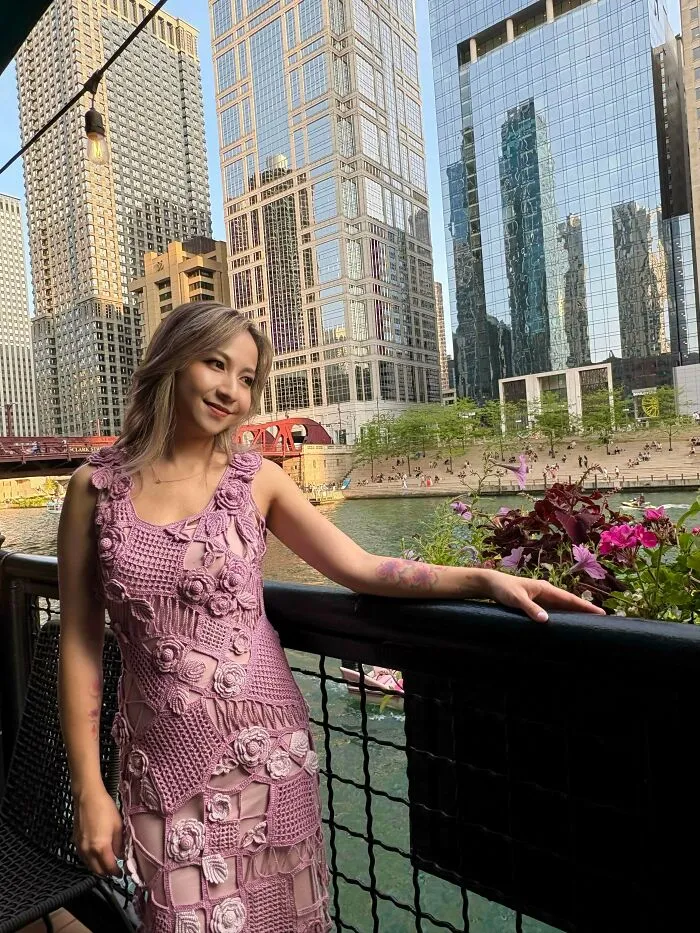 Woman wearing pink crochet dress posing by river in urban cityscape
