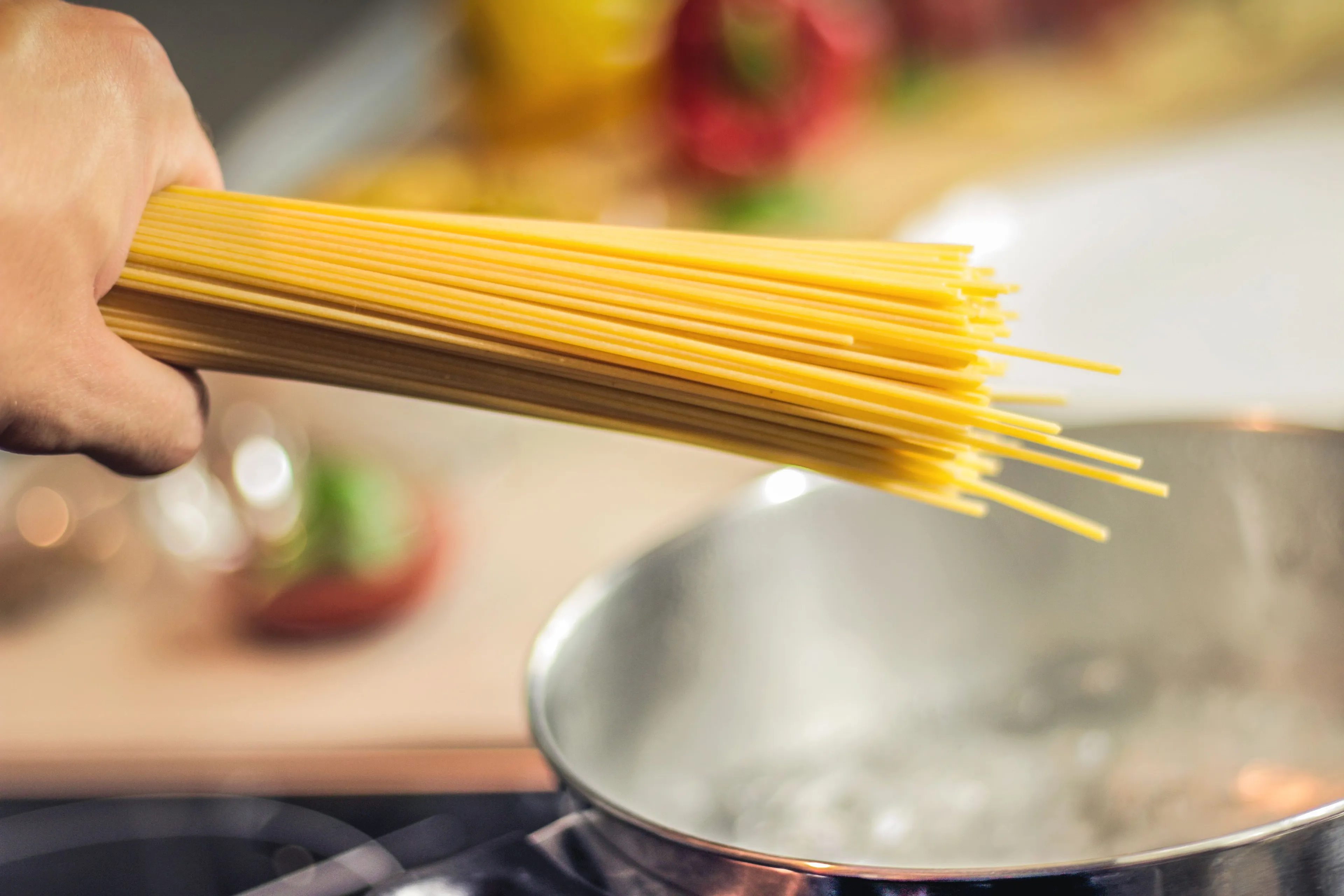 A hand holding uncooked spaghetti above a pot of boiling water, representing cooking as a hobby.