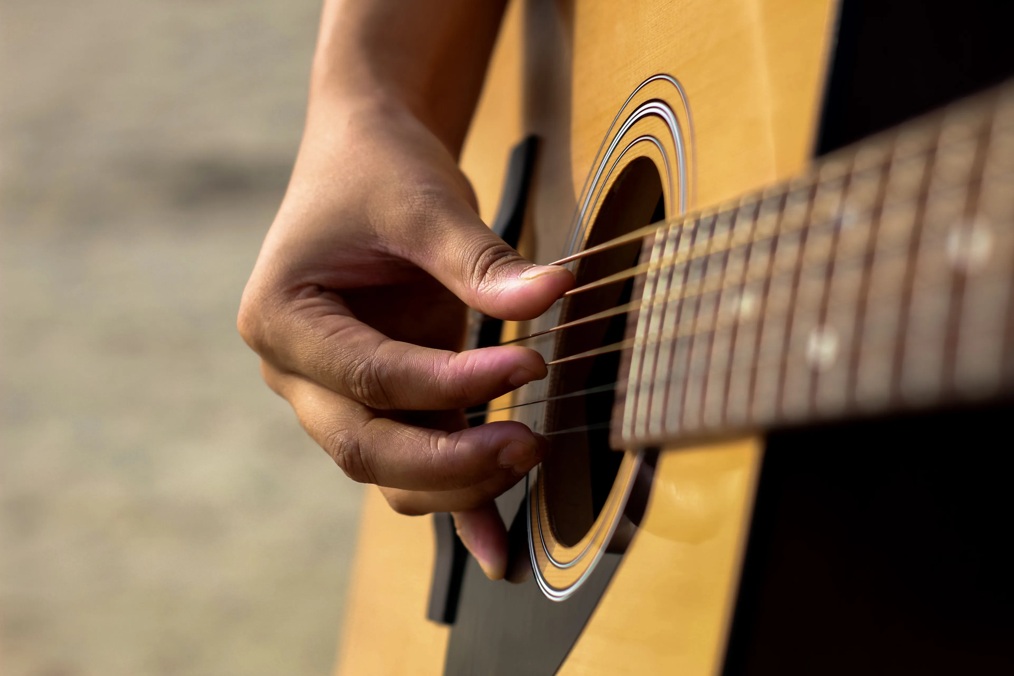 Close-up of a person's hand strumming an acoustic guitar, a hobby many enjoy playing.