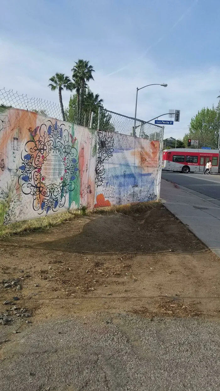 An artistic street mural on a fence, overlooking a street with a bus, promoting a clean environment without trash.