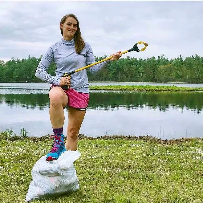 A woman stands triumphantly on a bag of collected trash, influencing others to clean up the world.