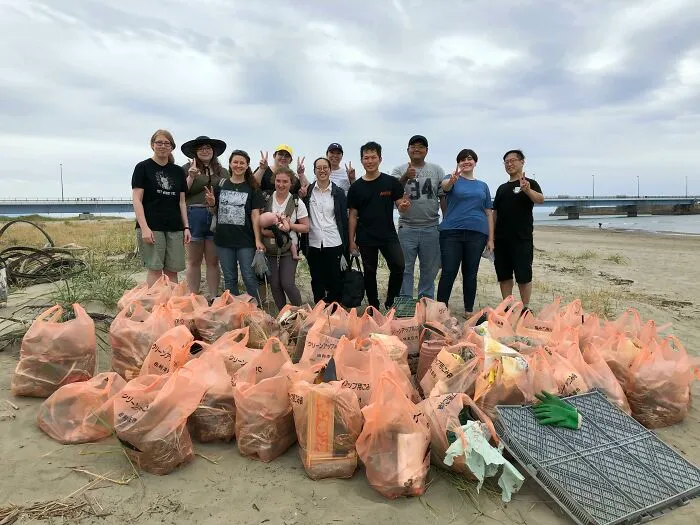Influencers clean up trash from the world, posing with bags of collected garbage on a beach.