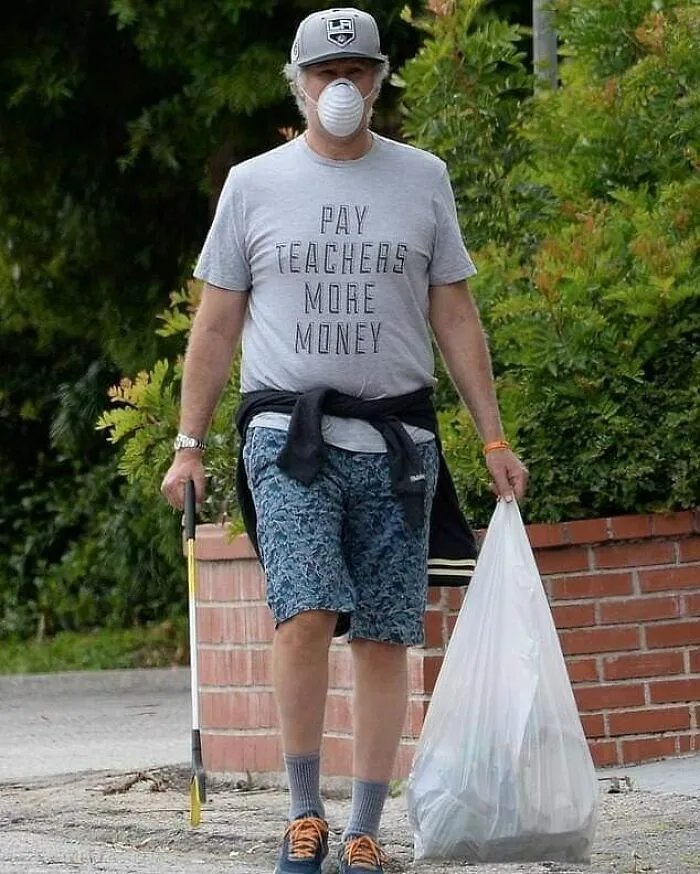 Man wearing a mask and a 'Pay Teachers More Money' shirt, holding a trash grabber and a bag of collected trash.