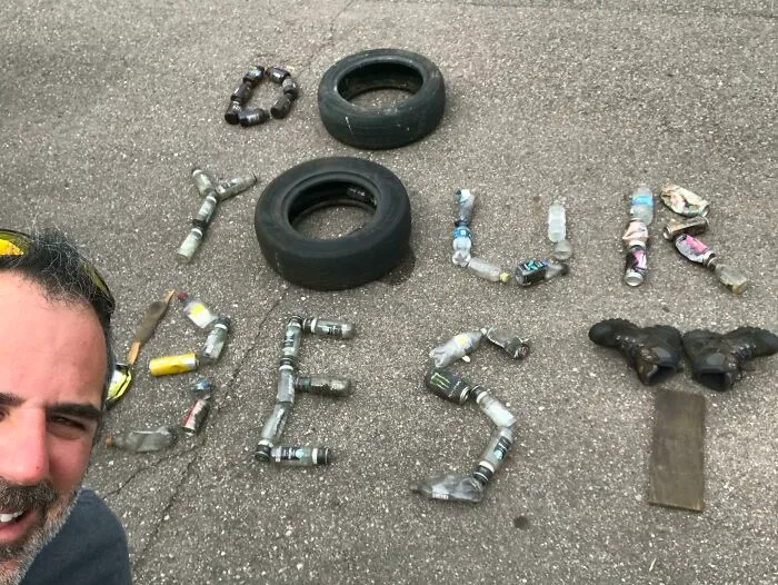 A man poses with trash arranged to spell out 'DO YOUR BEST', showcasing efforts against trash taking over the world.