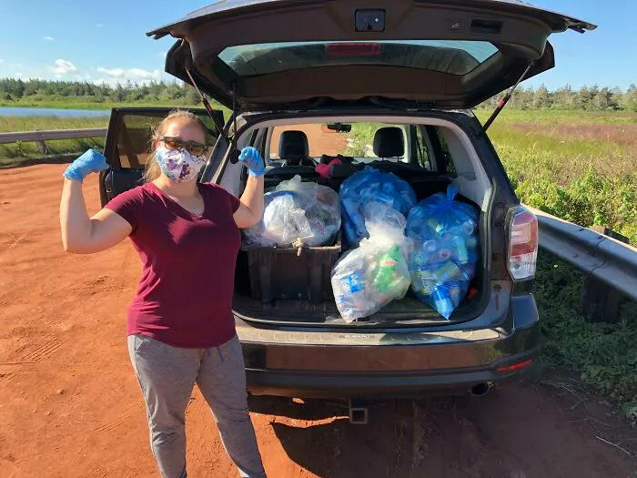 A woman wearing gloves poses beside a car filled with bags of collected trash, demonstrating efforts against trash taking over the world.