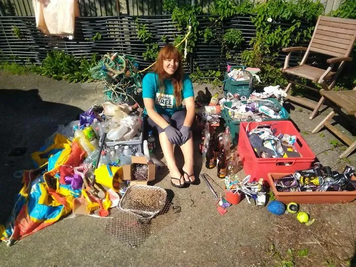 A smiling woman sits surrounded by collected trash, showing the impact of trash taking over the world.