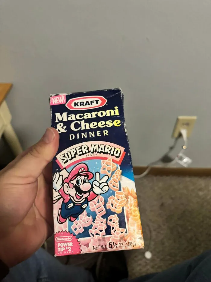 A hand holding old products: a vintage box of Kraft Super Mario Bros Macaroni & Cheese dinner.