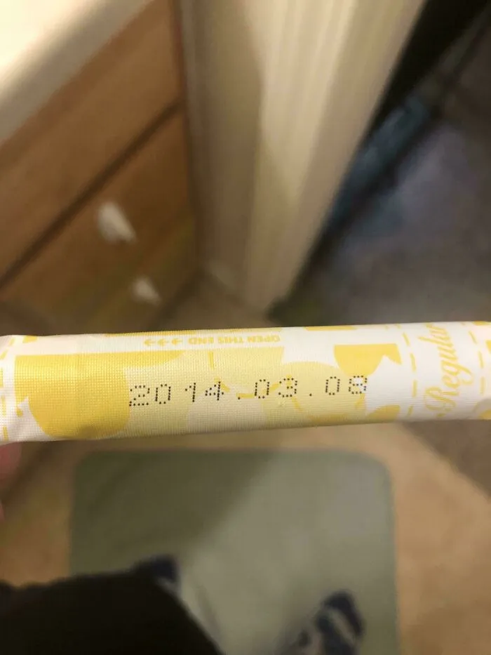 A closeup of a tampon wrapper showing an expiration date of 2014.08.08, an old product found at home.