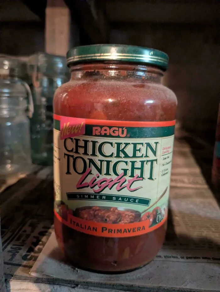 A dusty jar of Ragu Chicken Tonight Light Italian Primavera Simmer Sauce, an old product found at home.