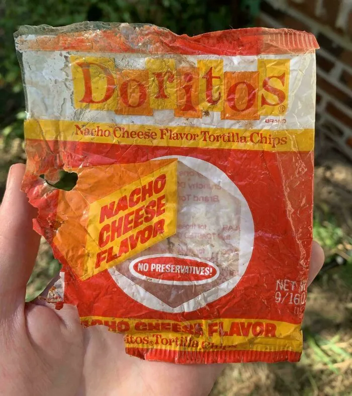 A hand holding an old, torn Doritos Nacho Cheese flavor tortilla chips bag, one of many old products found at home.