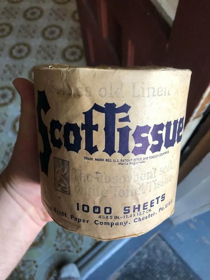 A hand holding an old roll of Scottissue toilet paper, an old product found at home that proves some people never throw anything away.