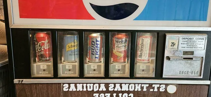 A vintage soda machine with cans of Coca-Cola, Schweppes, Bud Light, Welch's, and Budweiser. Old products people found.