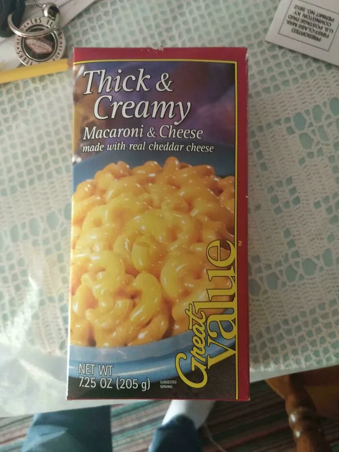 A box of Great Value Thick & Creamy Macaroni & Cheese, an old product, sits on a patterned tablecloth.