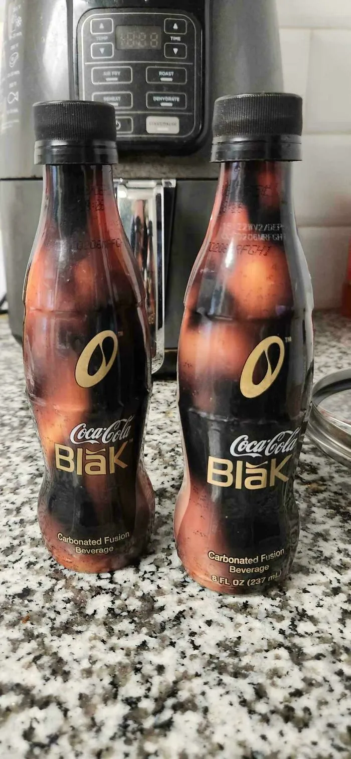 Two bottles of old products, Coca-Cola Blak, a carbonated fusion beverage, sit on a speckled countertop.