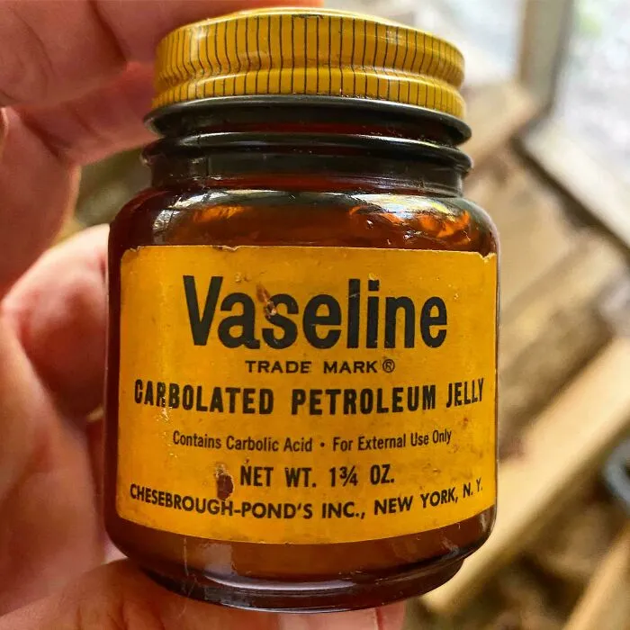 A hand holds a small, old jar of Vaseline, an old product found at home.