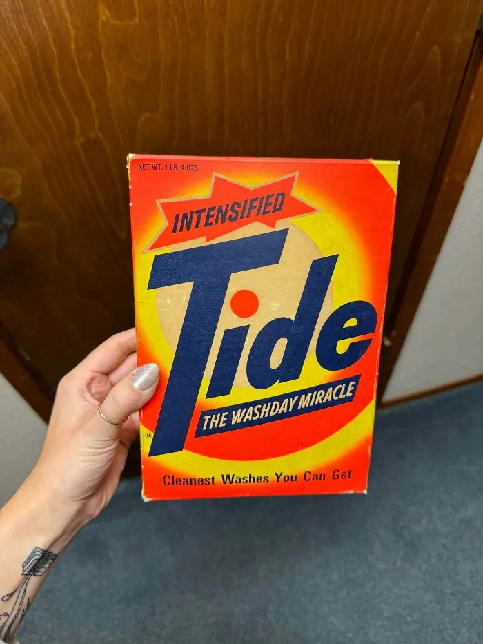 A hand holding an old, unopened box of Intensified Tide detergent, an old product people found at home.