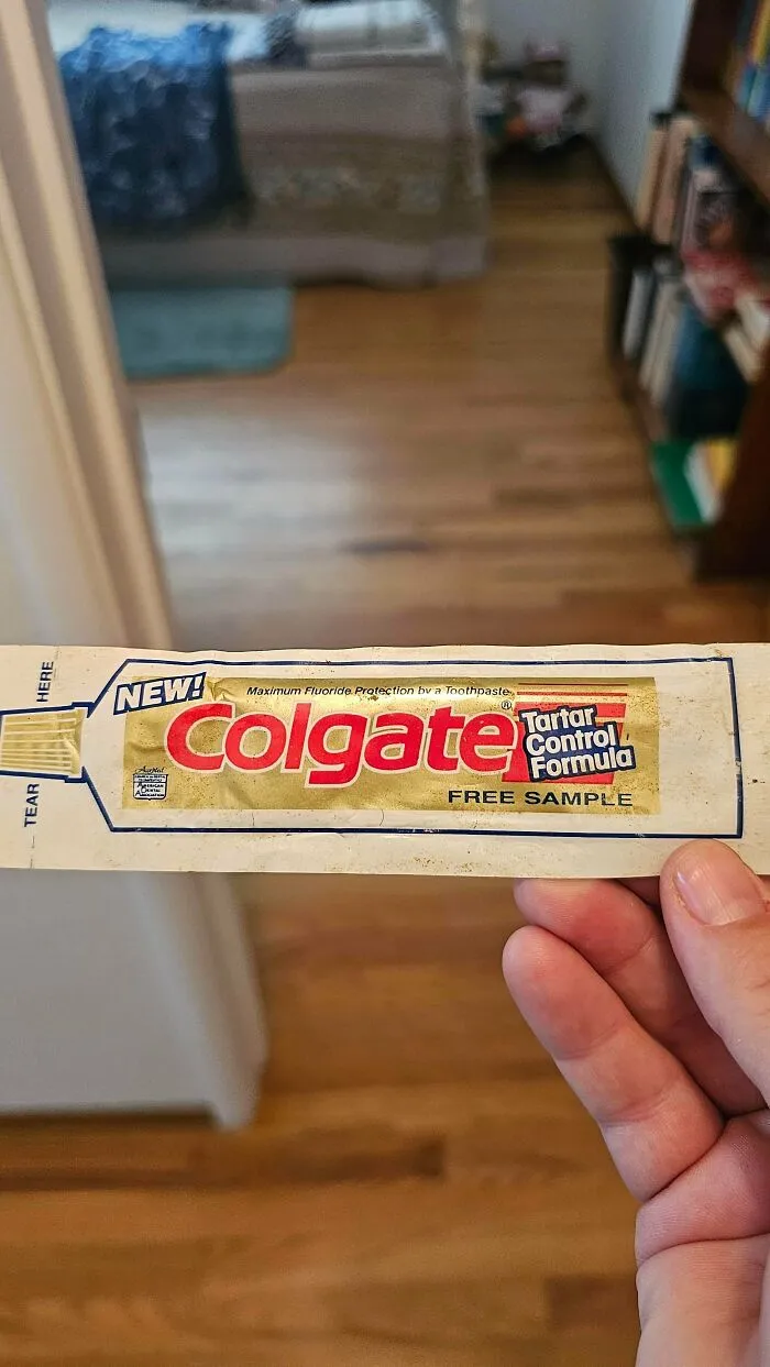 A hand holding a vintage Colgate free sample toothpaste packet, one of many old products found at home.