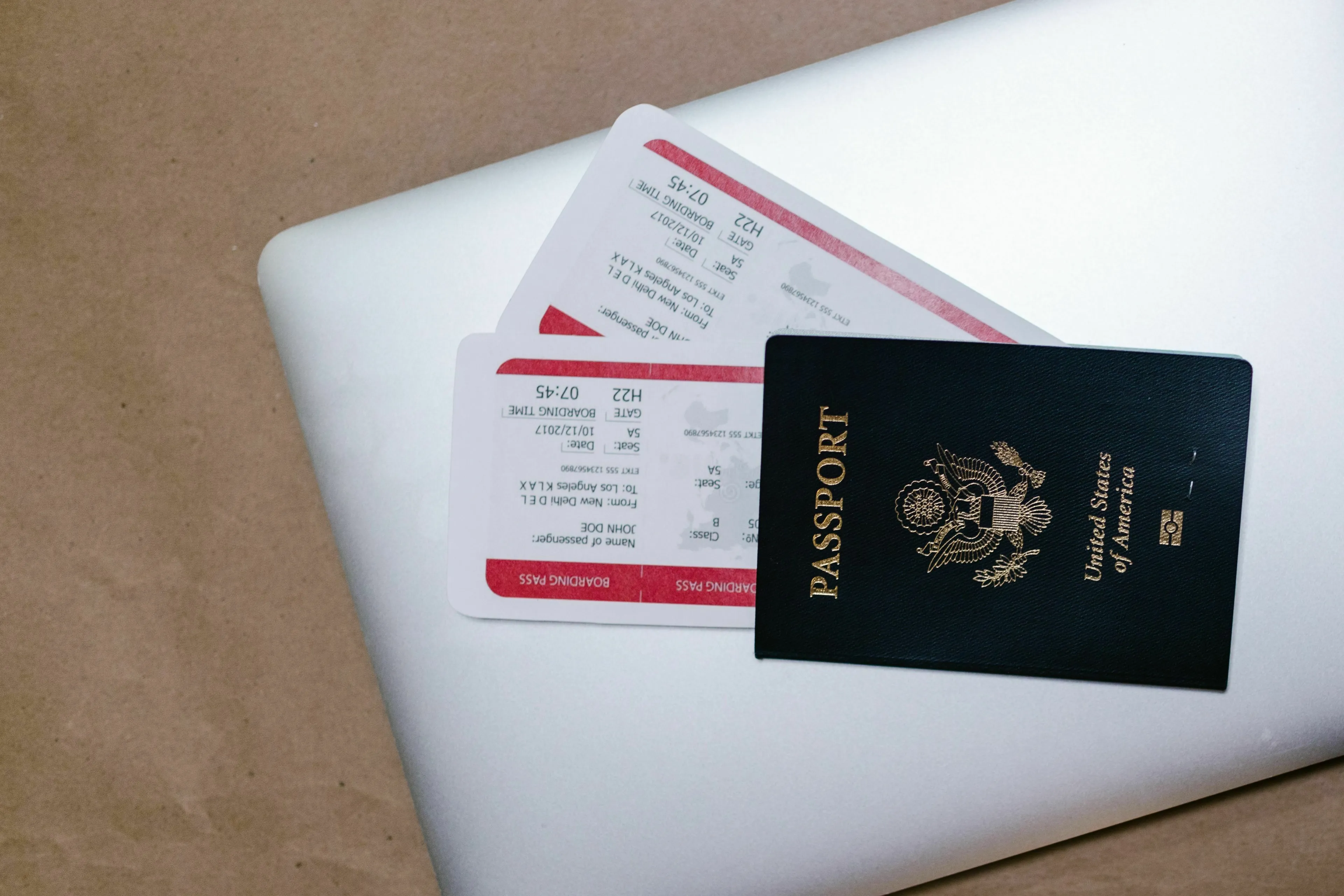 A US passport and two airline tickets resting on a laptop. American vs British English words.