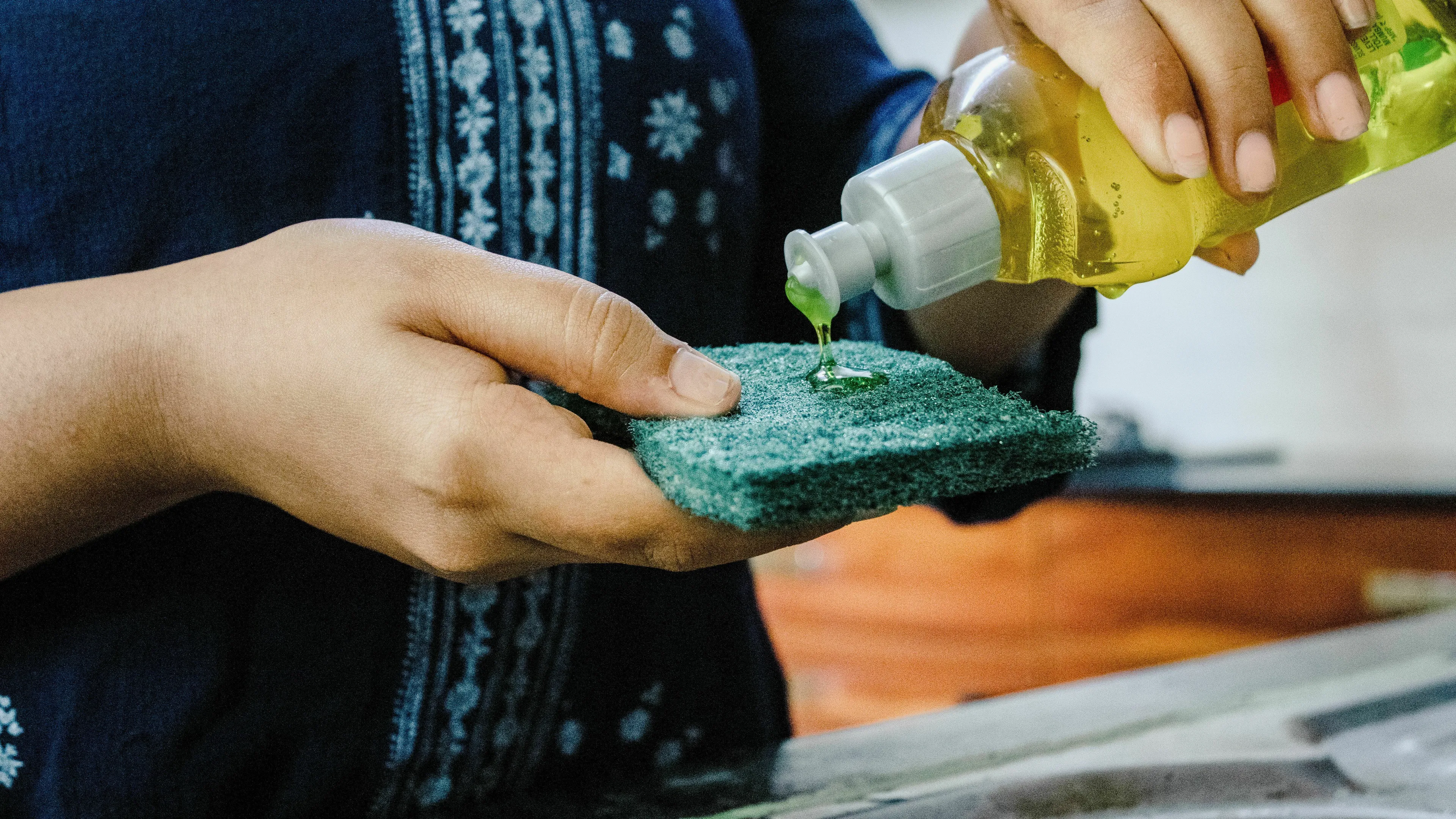 Hands pouring dish soap onto a sponge, highlighting British English words for household products.