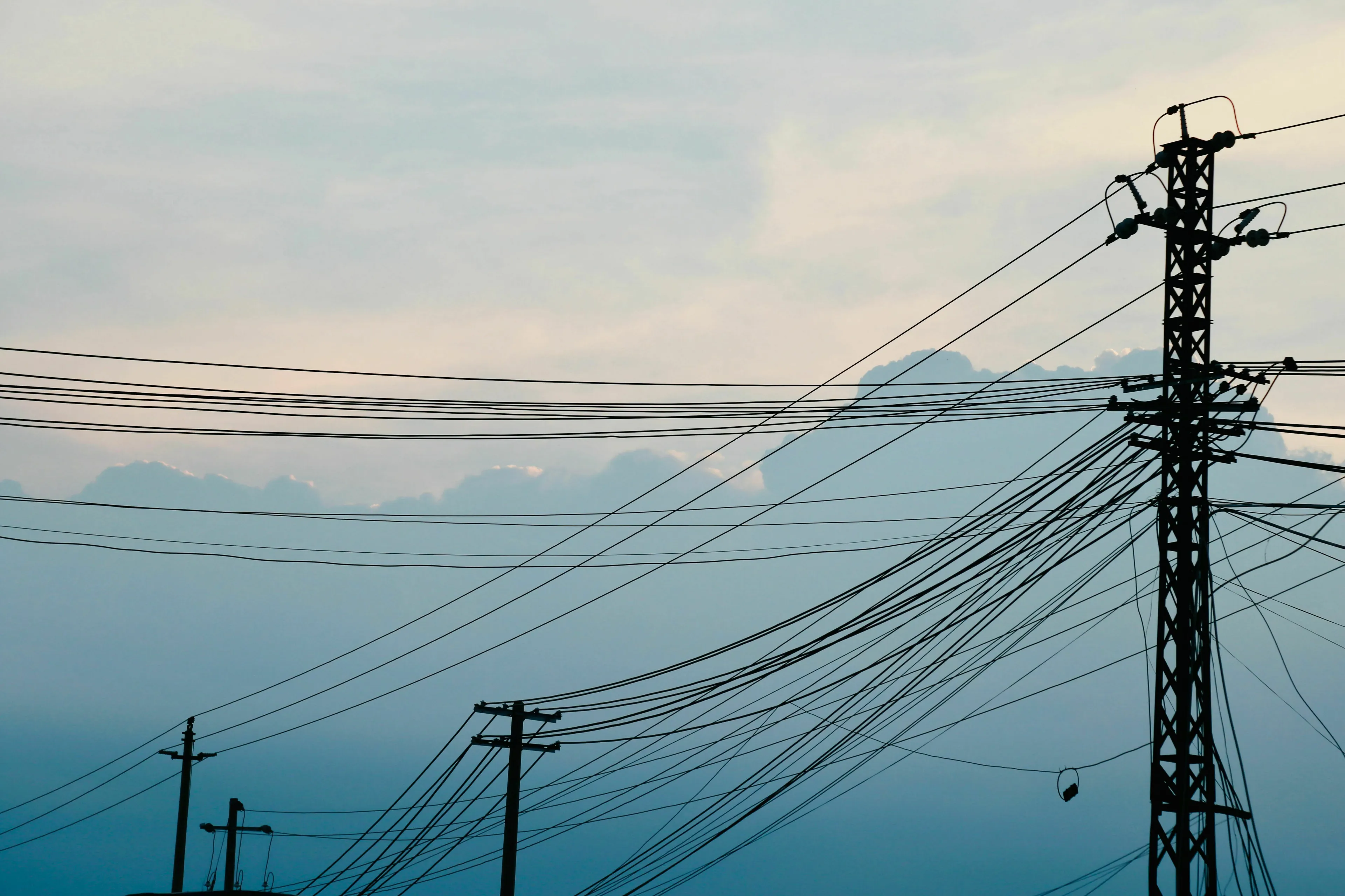 Silhouette of power grid lines against a cloudy sky, depicting a power grid failure or dystopia.