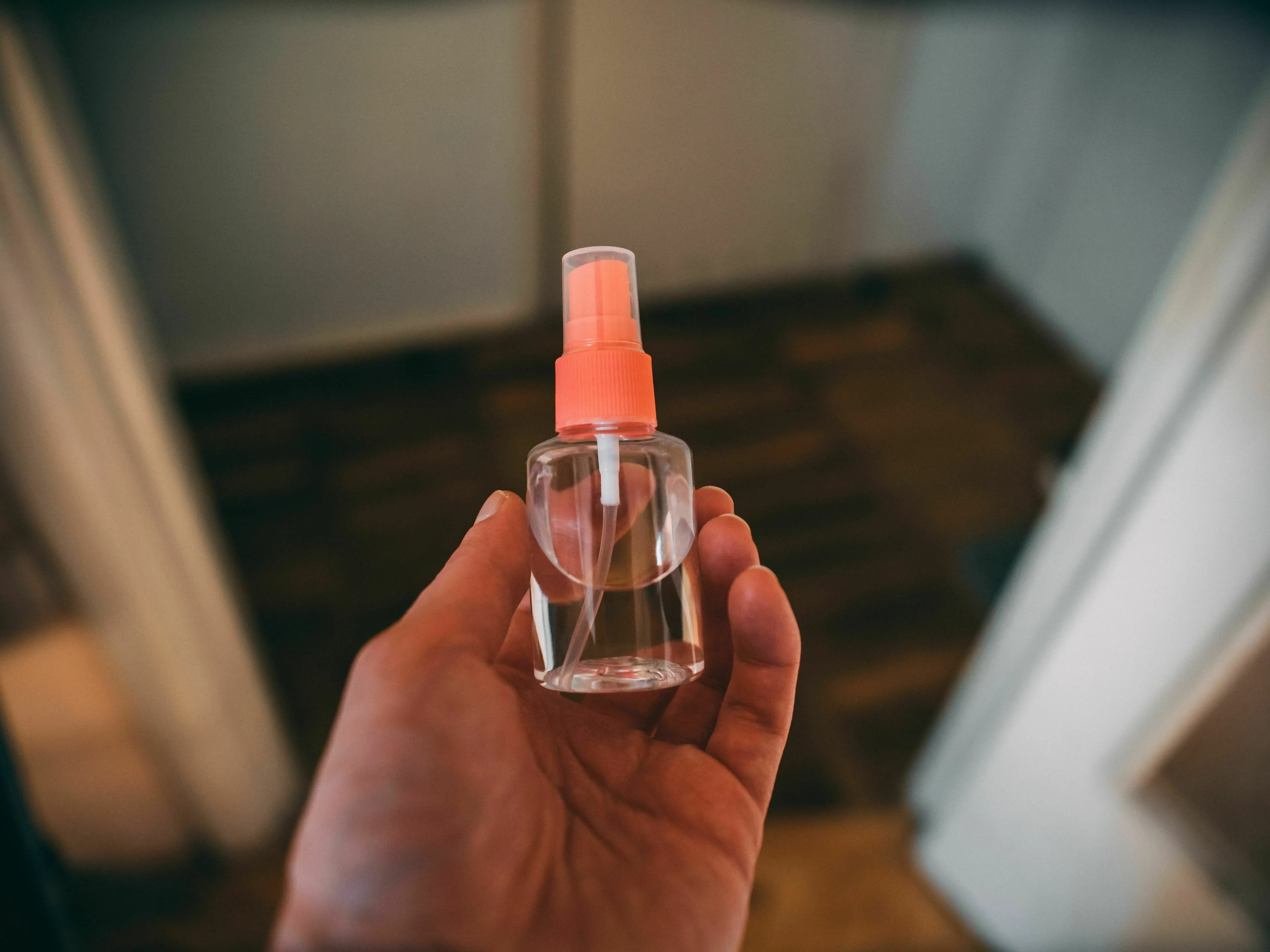 Hand holding a small clear spray bottle, representing a forbidden item one might smuggle in.