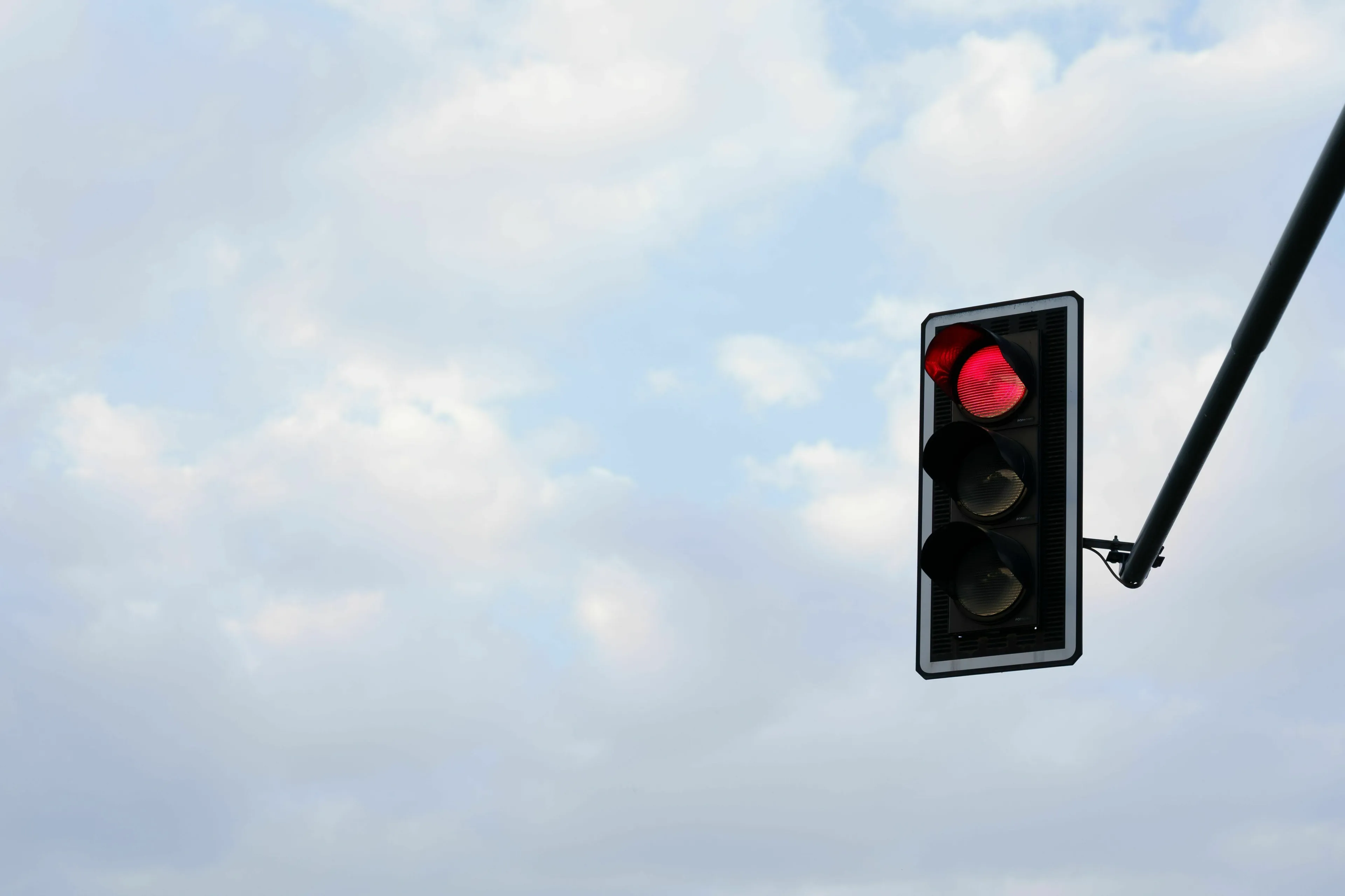 Red traffic light against a cloudy sky, symbolizing a rule one might break in a utopia or dystopia.
