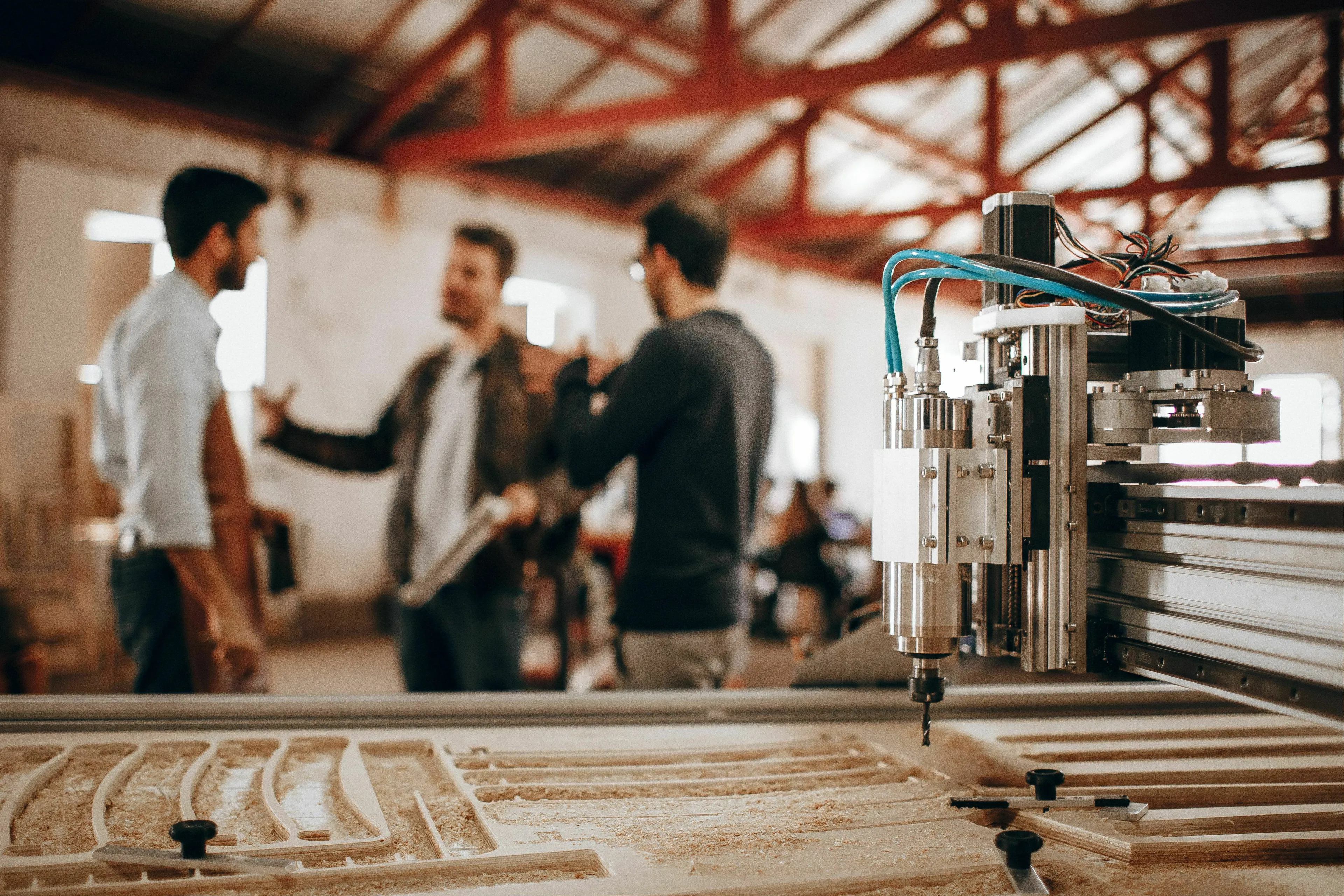 A machine making big decisions for you, three men discussing work in a factory with a CNC machine in the foreground.
