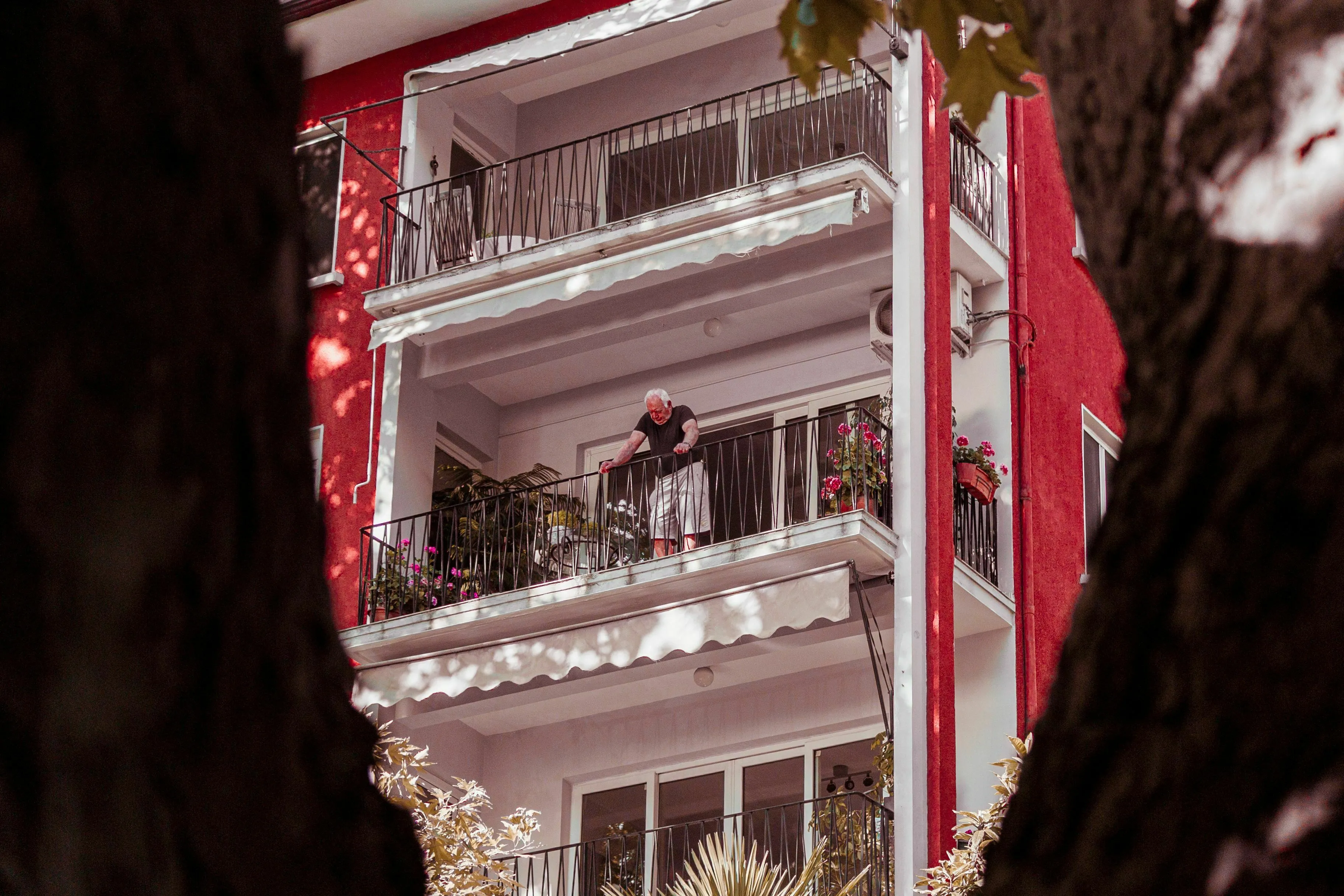An elderly woman standing on a balcony of a red apartment building. Neighbor conflict.
