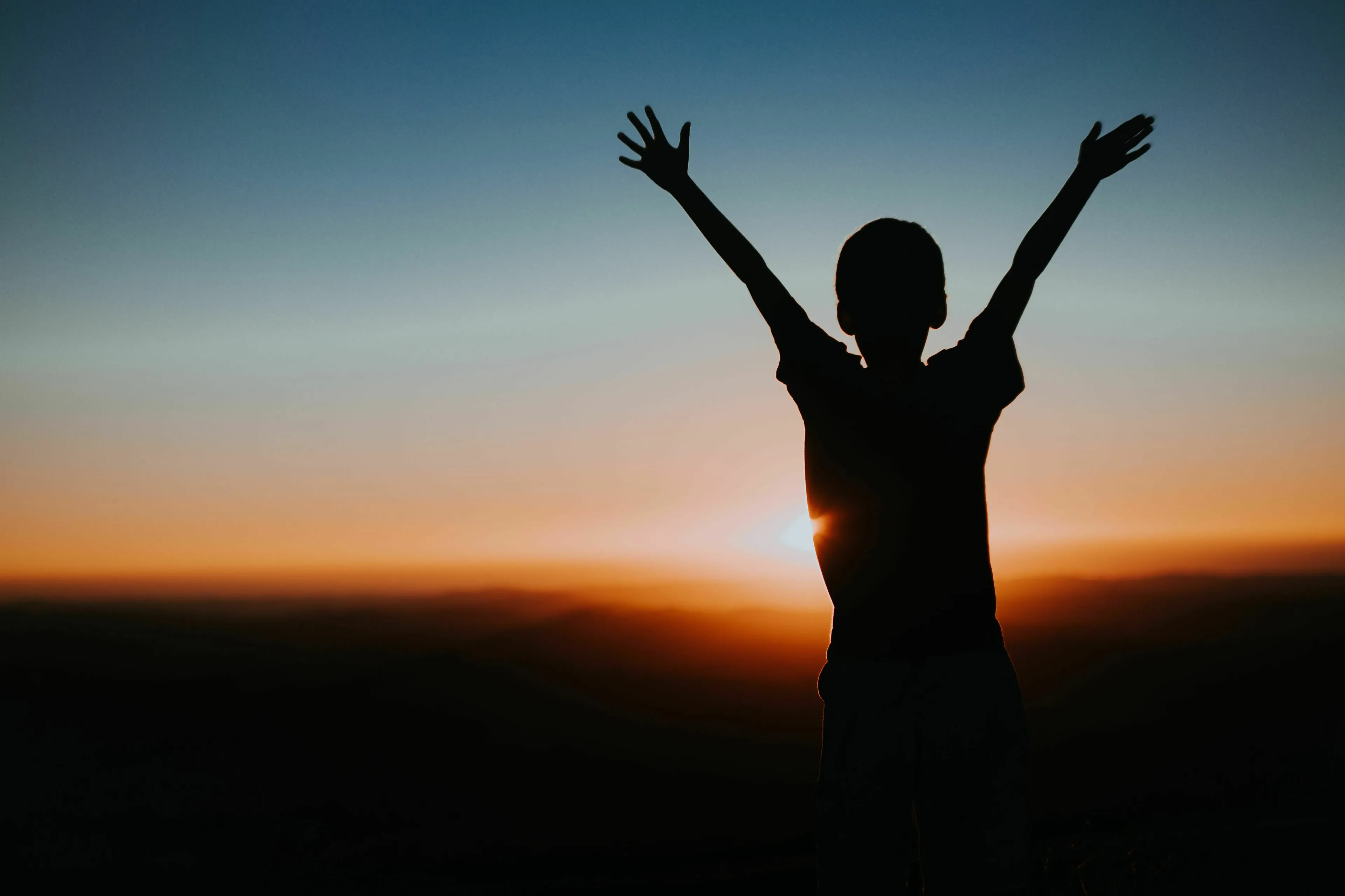 Silhouette of a child with arms raised against a sunset. Raising kids worries.