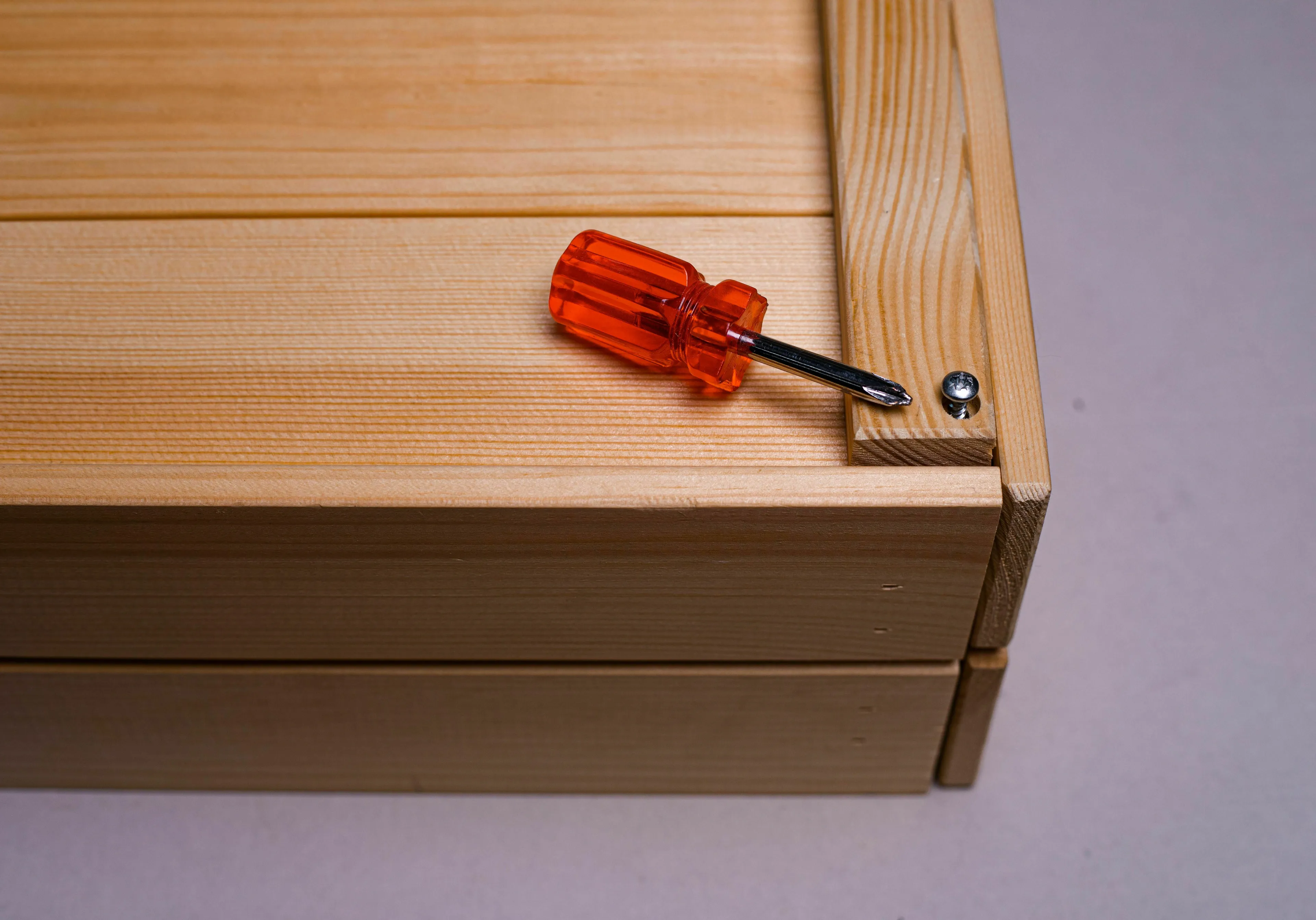 A small screwdriver next to a screw in a wooden box, symbolizing extra labor in a utopia or dystopia.