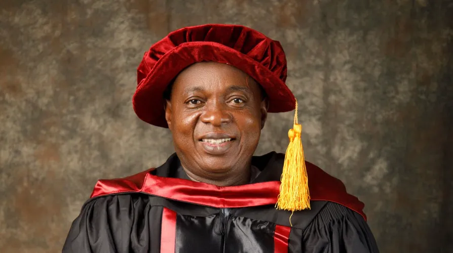 A smiling man in academic regalia, representing the person in charge of a school in American English.