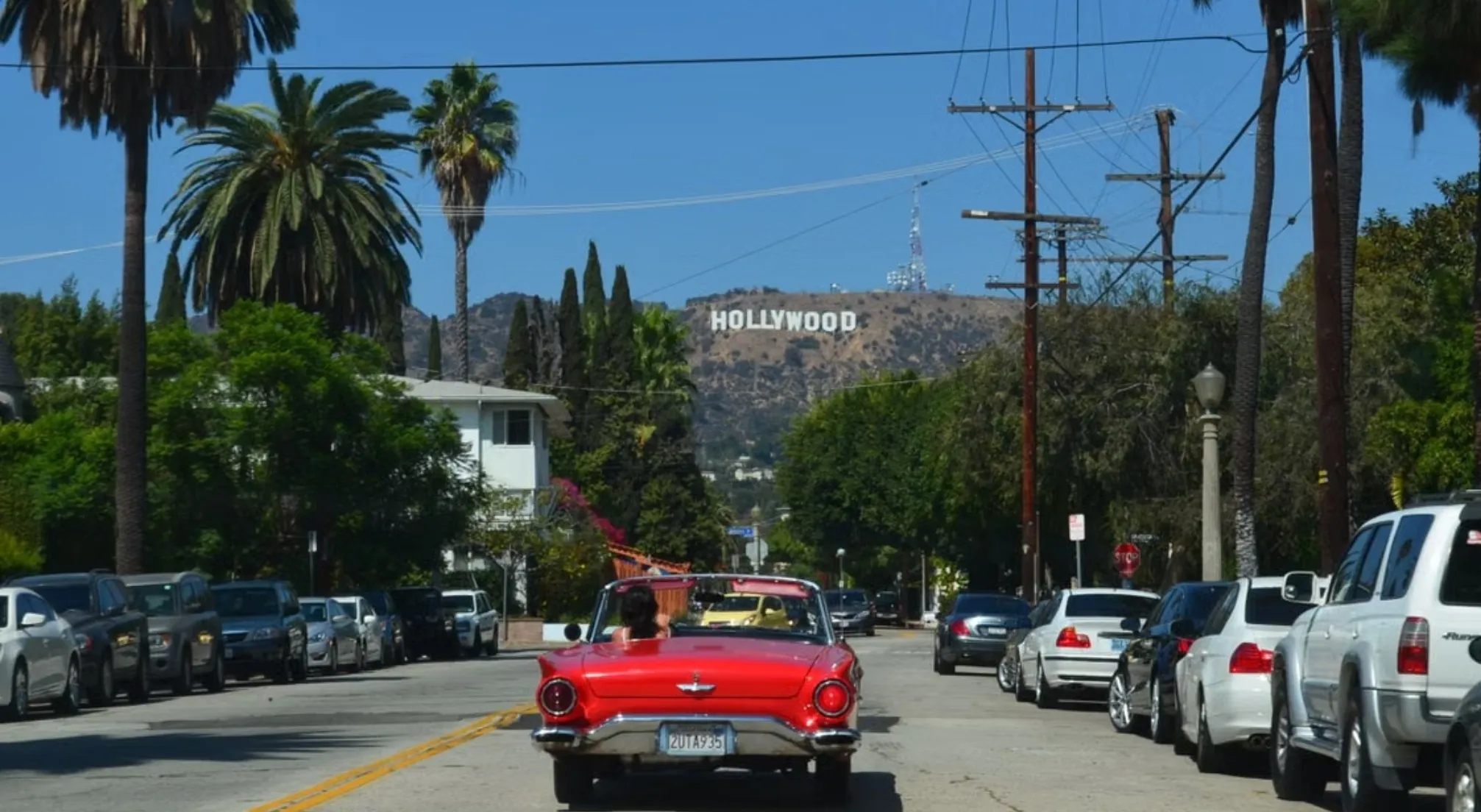 Red convertible driving towards the Hollywood sign, illustrating Los Angeles' history as a haven for filmmakers.