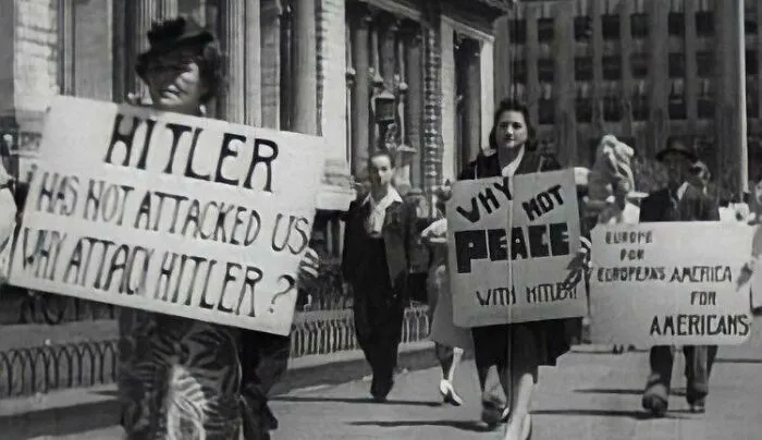 A historical photo showing people protesting against war, holding signs that read 'Why not peace'.