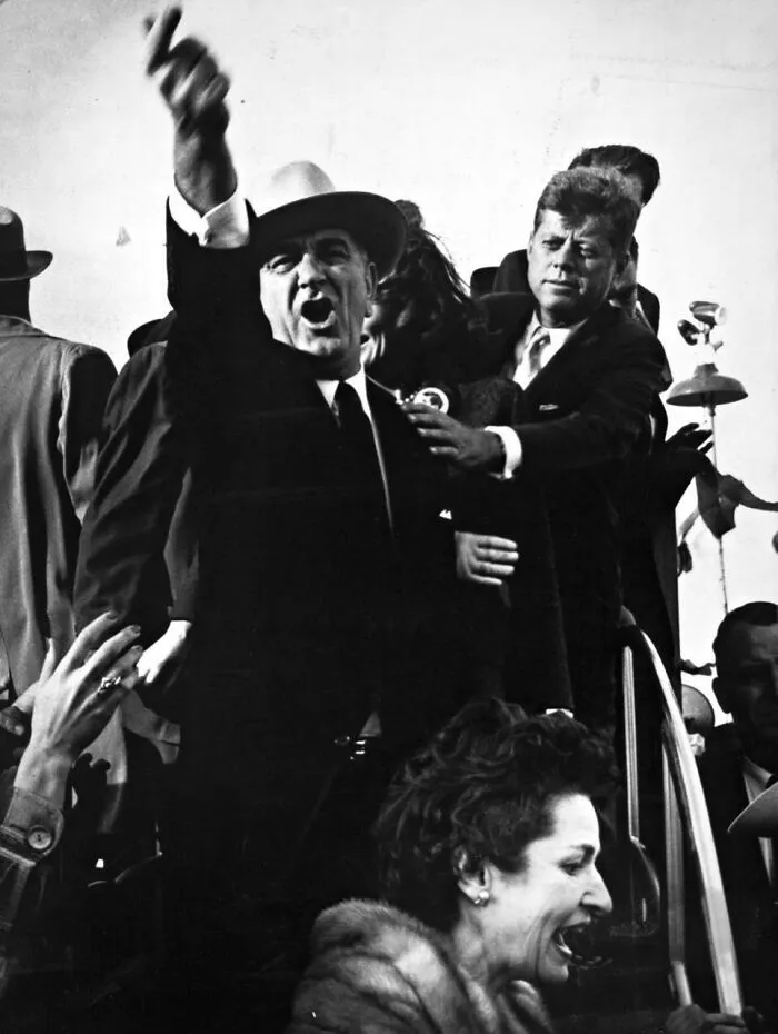 Heartbreaking photo from history showing Lyndon B. Johnson with his arm raised, with John F. Kennedy behind him.