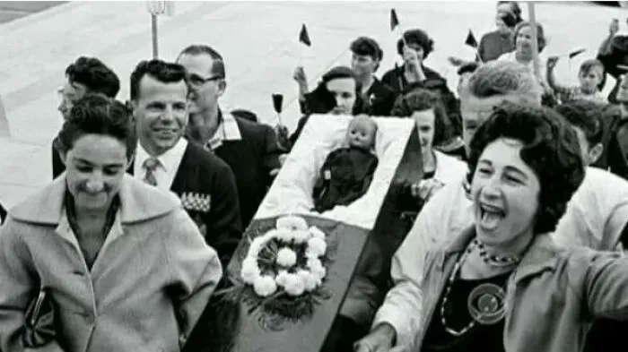 People smile and cheer while carrying a small coffin containing a doll, a curious and beautiful photo from history.