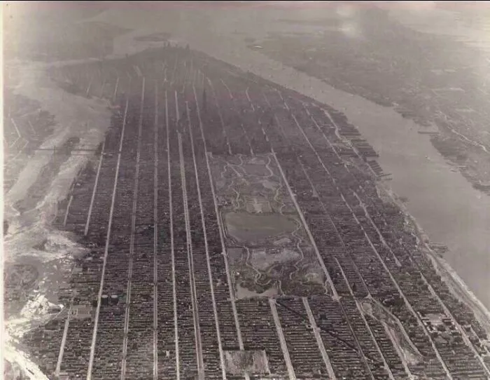 An aerial view of a sprawling city, crisscrossed with streets and featuring a central park, an interesting photo from history.