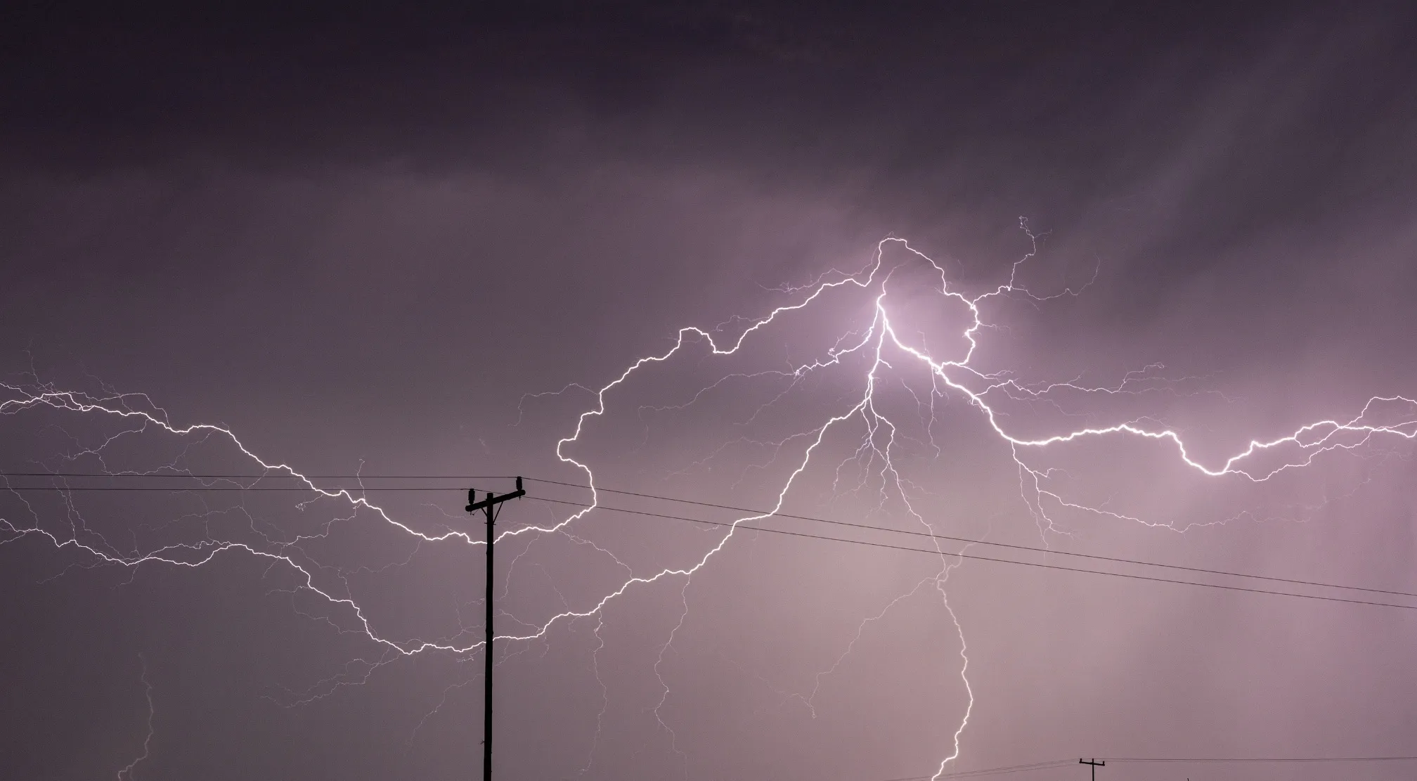 A bright lightning strike illuminates a dark, stormy sky over power lines. Elementary school true or false?