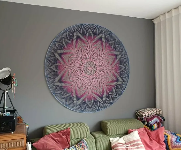 Large crochet wall hanging with pink and blue floral design in living room