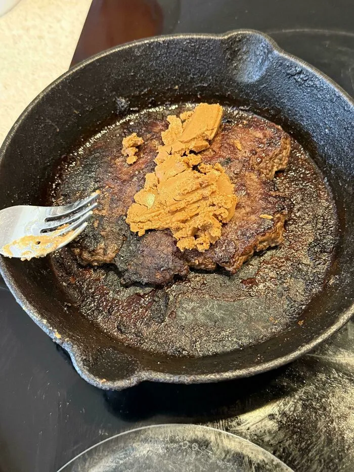 Questionable food combos showing a burger patty topped with peanut butter in a pan.