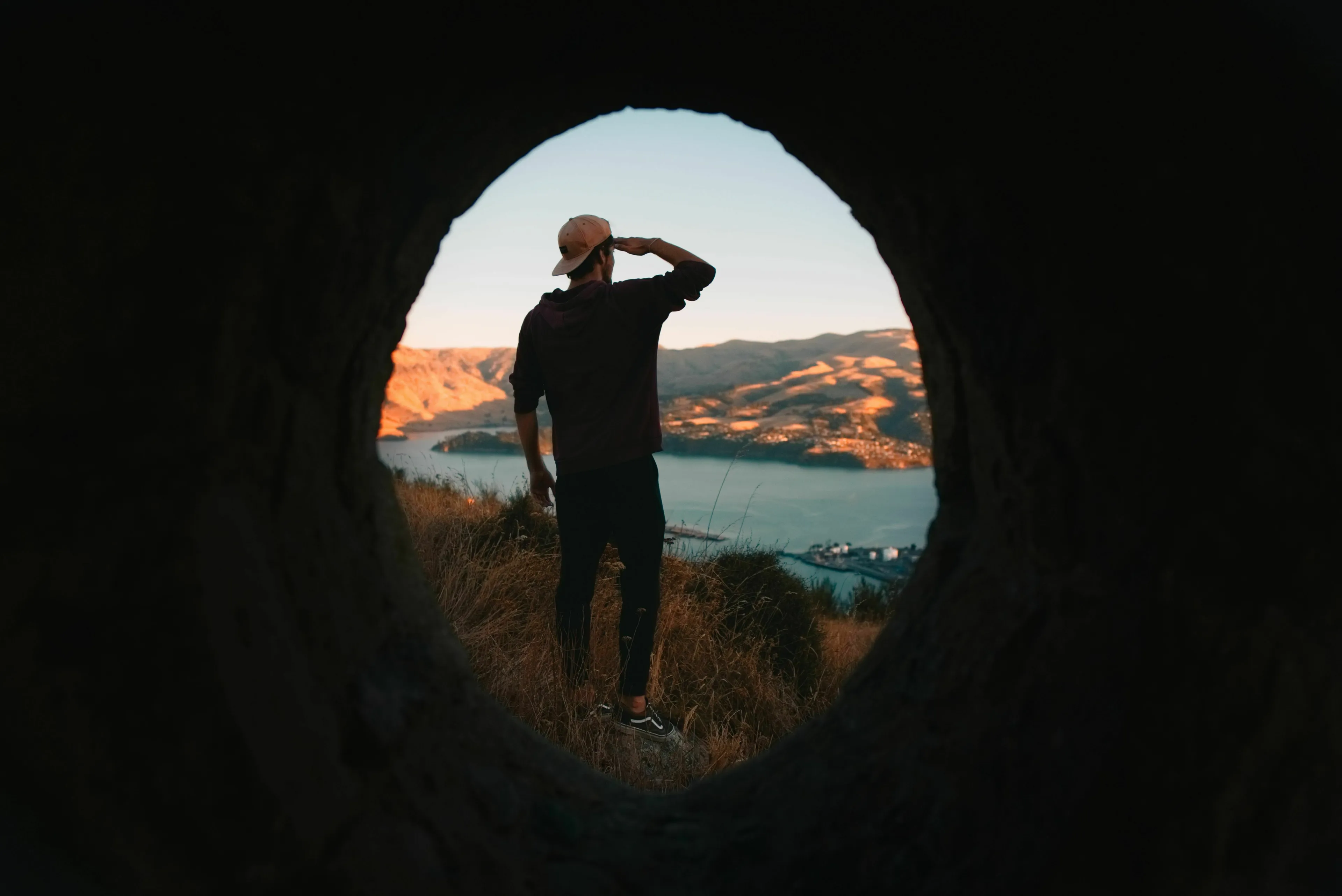 A man looking out at a scenic bay from a cave opening, depicting the action to seek something.